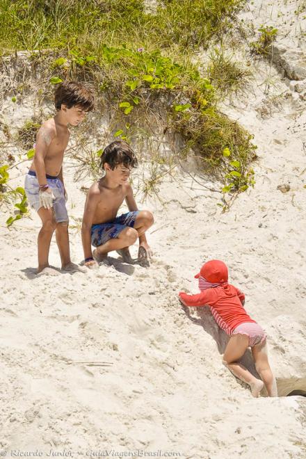 Imagem de três crianças brincando nas areias da Praia Pontal do Atalaia.